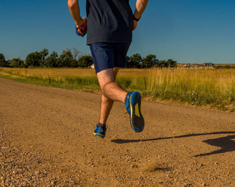 Un uomo che corre su una strada sterrata aperta in una giornata di sole con le sue scarpe HFS II a piedi nudi.
