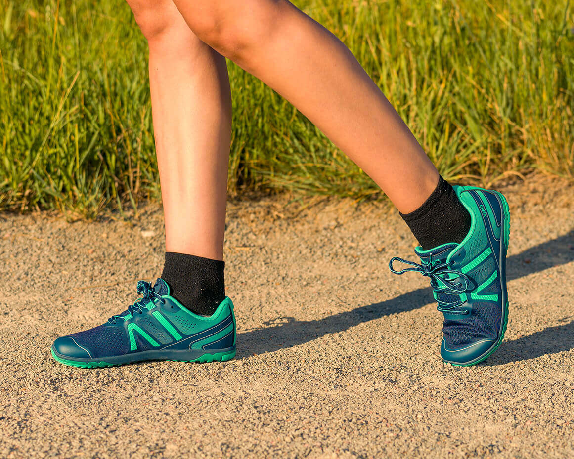 A close up shot of a woman walking in her HFS II barefoot shoes on a dirt road