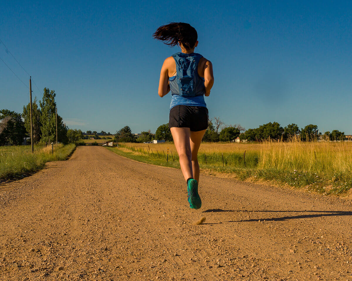 A woman running down an open dirt road on a sunny day in her HFS IIs