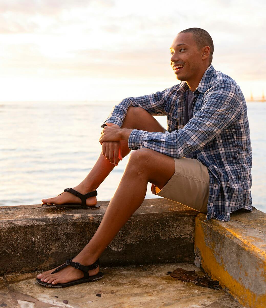 En leende man som sitter vid vattnet med sina H-Trail-sandaler