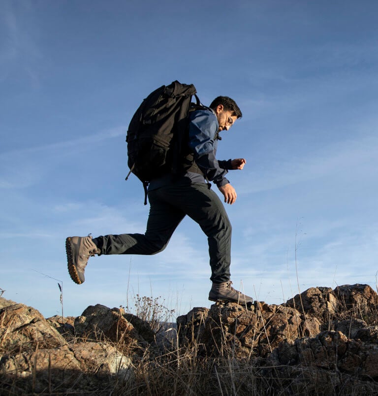 A man wearing Scrambler Mid II boots leaping from one rock to another outside on a hike