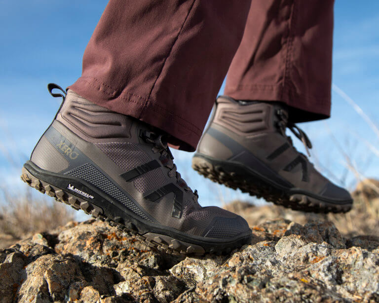 Une femme portant des bottes Scrambler Mid II se déplaçant avec vigueur sur un terrain rocailleux.