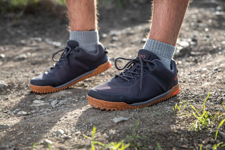 Gros plan sur un homme portant des chaussures Rideway Mesh Low, debout sur le sentier, au soleil.