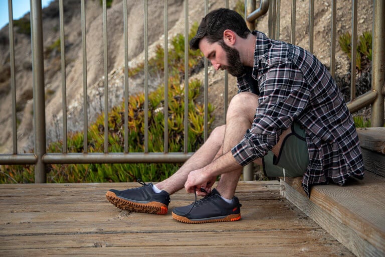 Een man zit buiten op een houten terras en trekt zijn Ridgeway Mesh Low schoenen aan.