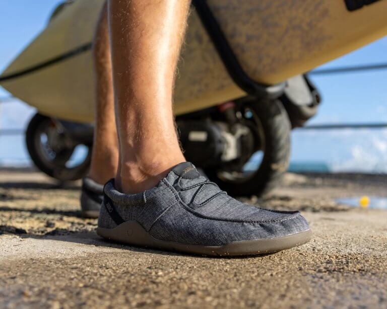 Vue inférieure de la jambe d'un homme portant des chaussures de plage Kona, debout devant un chariot de planche surf .