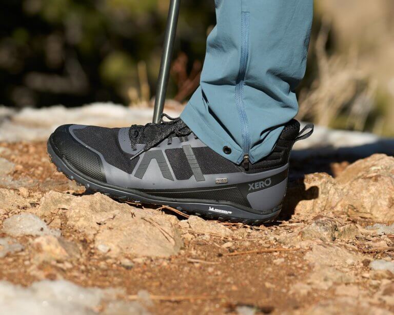 A man wearing Scrambler Mid II WP boots standing outside on a dirt trail with a trekking pole