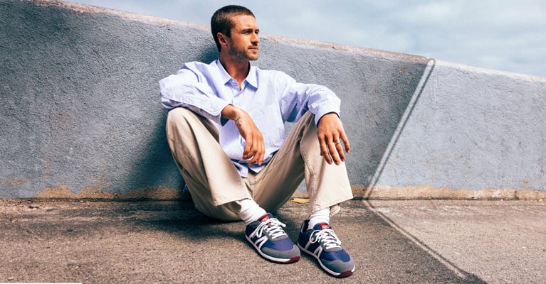 Young man sitting against a concrete wall wearing the Wynn sneaker